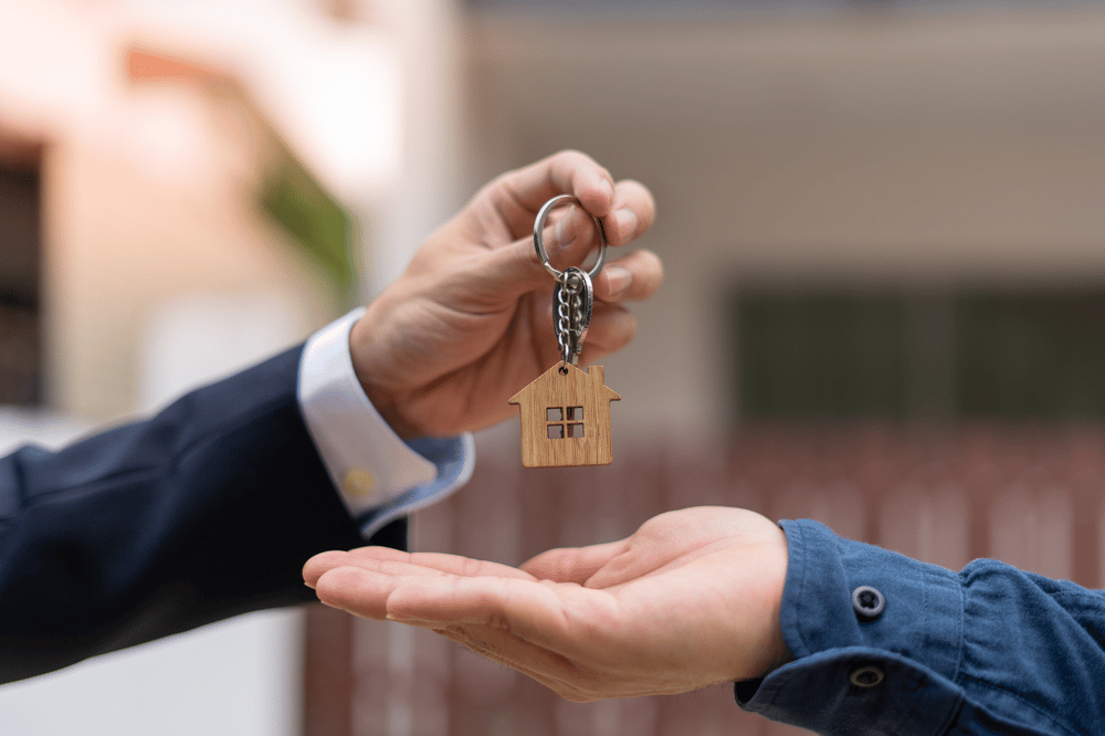 A house-shaped keychain is handed from one person to another.