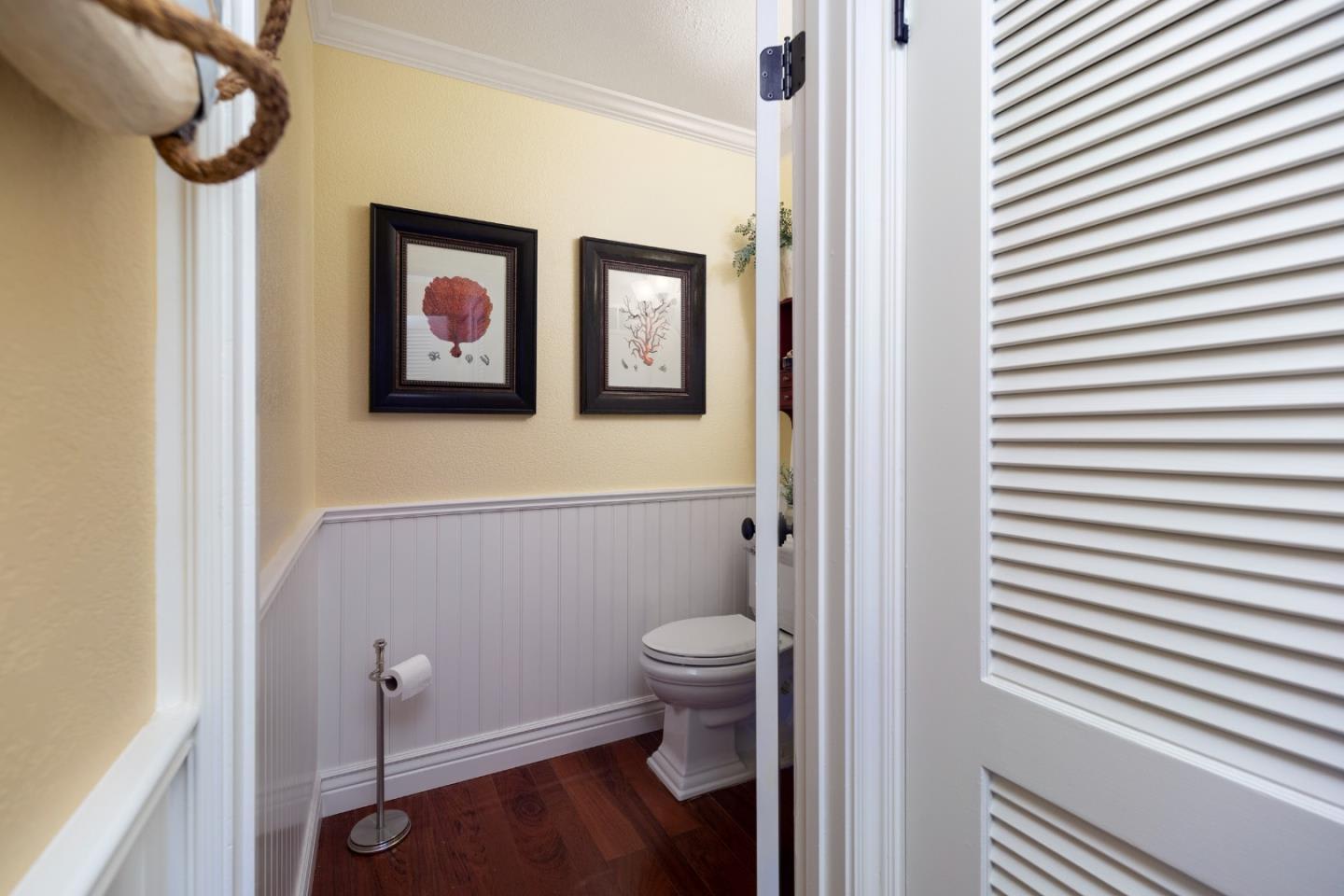 Powder room with framed botanical prints, white beadboard wainscoting, and a dark wood floor.