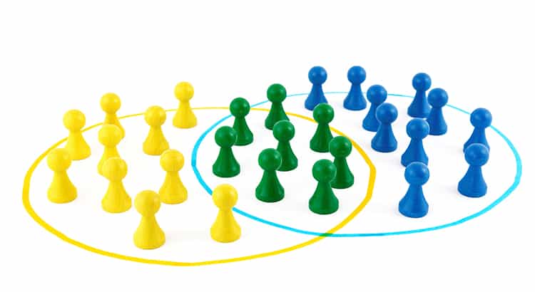 There are yellow, green, and blue pawns. The yellow and blue pawns are grouped within their respective colored circles, while the green pawns are placed in the area where the two circles overlap. This image seems to visually represent a concept of intersection or shared attributes between two groups, often used to illustrate ideas related to Venn diagrams, teamwork, collaboration, or overlapping interests.