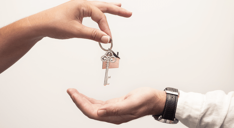 A close-up of two hands exchanging a set of keys. One hand, wearing a watch, is handing the keys over to the other, symbolizing a transaction or transfer.