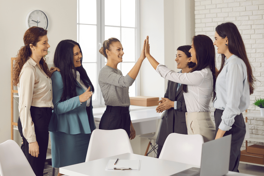 Women celebrate a negotiation with a high-five in a bright office.