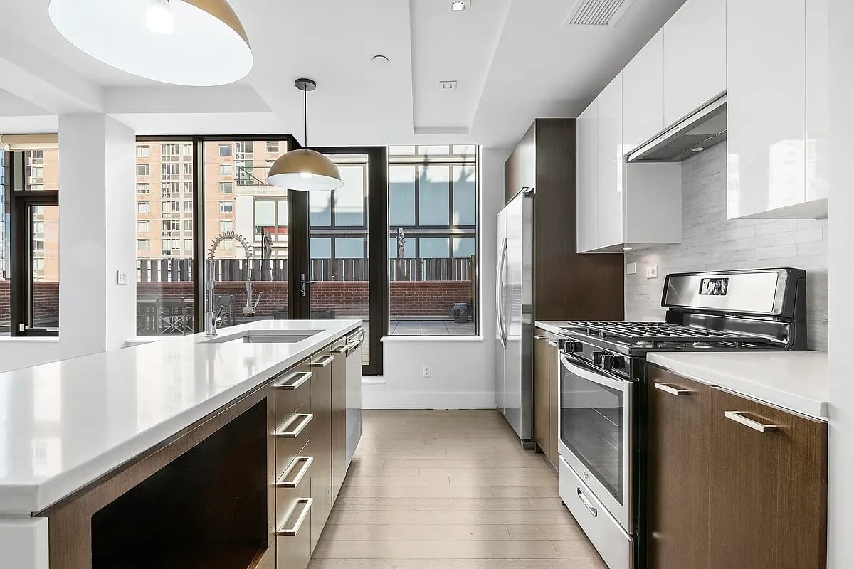 Modern kitchen with a long white island, dark wood cabinets, and stainless steel appliances.