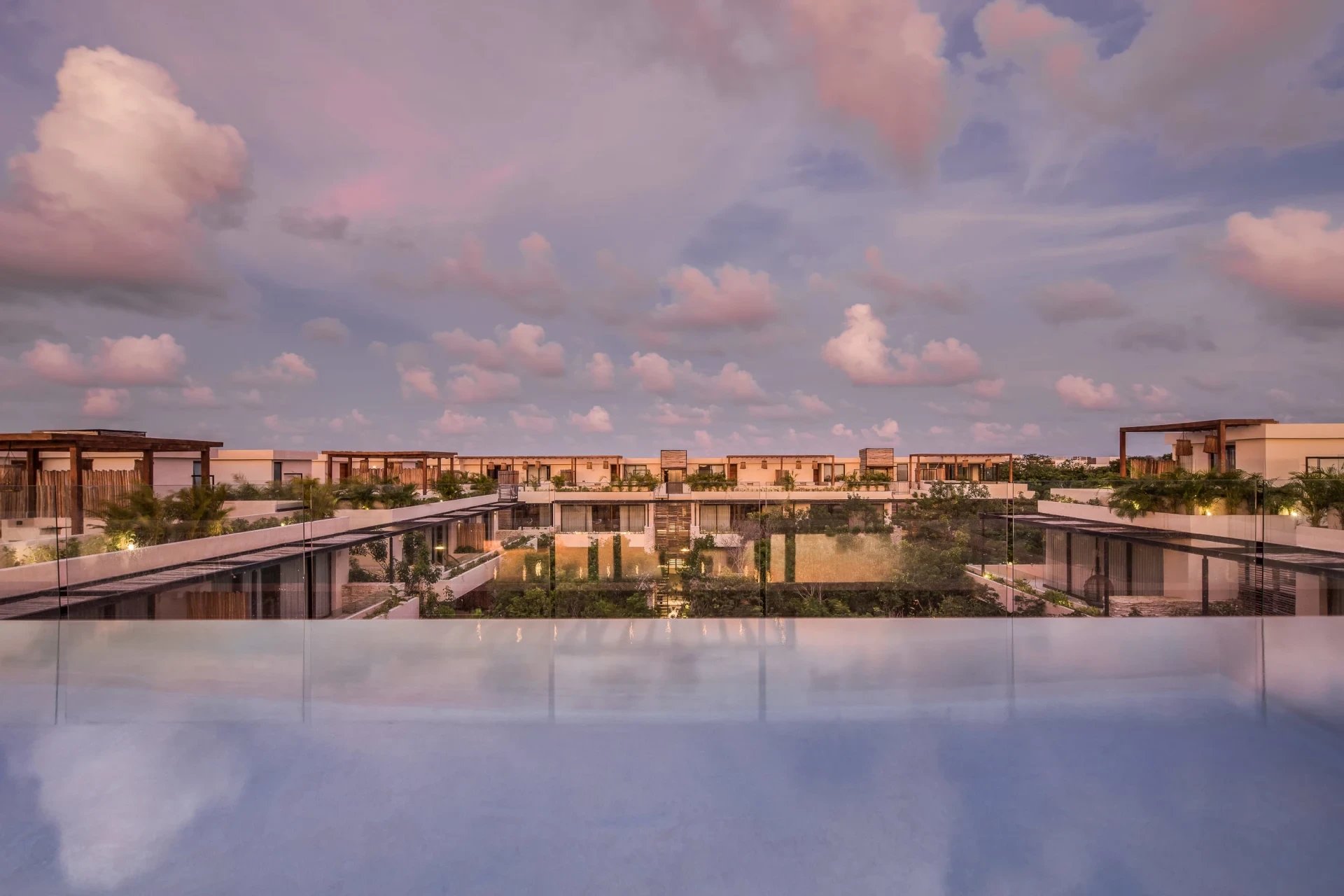 Modern condo-hotel buildings and landscaped courtyard seen from a rooftop pool at sunset.