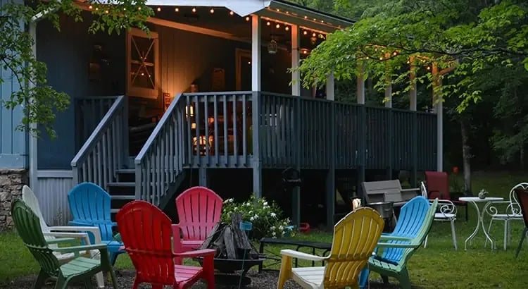 An inviting outdoor scene with a wooden deck and colorful Adirondack chairs. String lights are hung, suggesting an evening gathering or a place to relax outdoors.