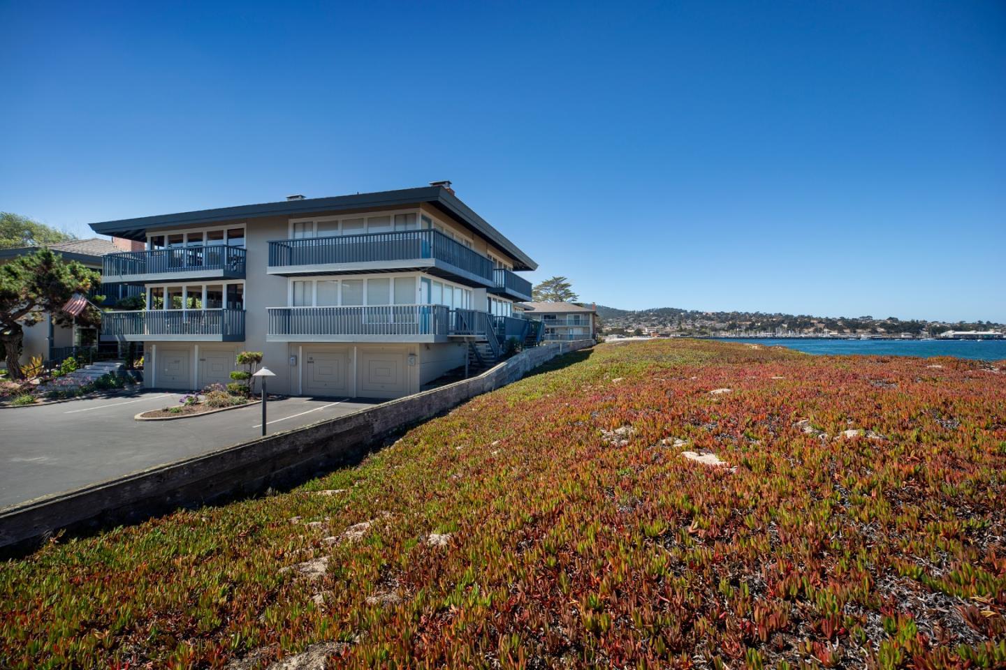 Coastal multistory home with wraparound balconies beside the ocean and a planted shoreline.