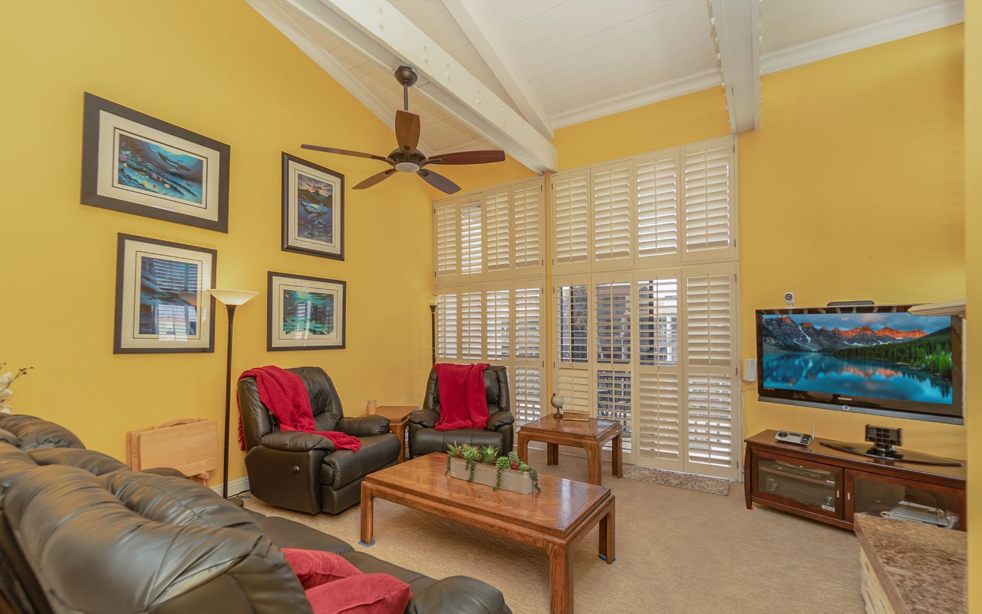 Living room with yellow walls, vaulted ceiling, plantation shutters, and leather seating.