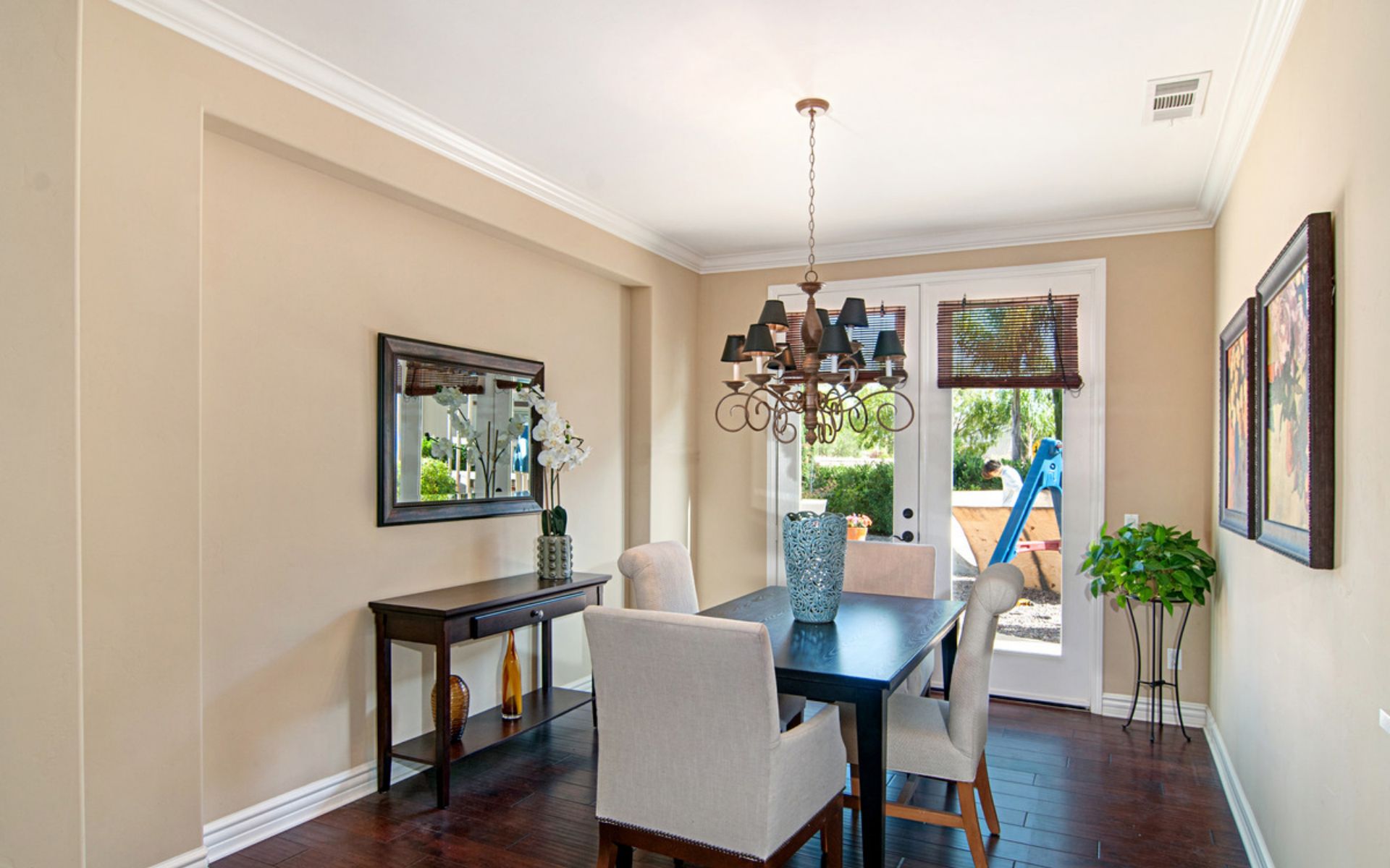 Dining room with a dark wood table, pale chairs, chandelier, and glass doors to the garden.