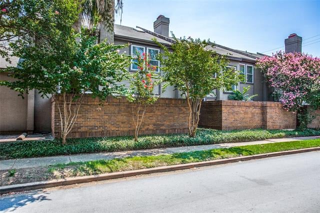 Gray residential building behind a brick wall, framed by leafy trees and pink blossoms.