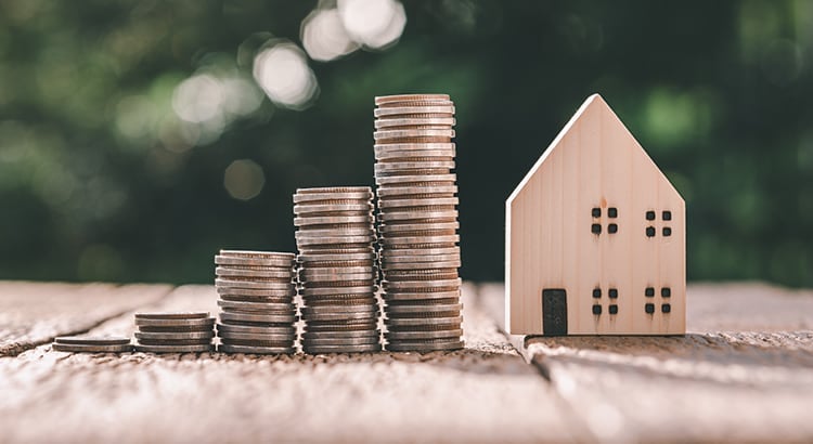 A stack of coins and a small house model, symbolizing home ownership and financial investment.