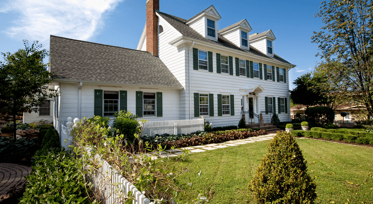 A charming white house with green shutters surrounded by a vibrant garden, showcasing a serene and inviting atmosphere.