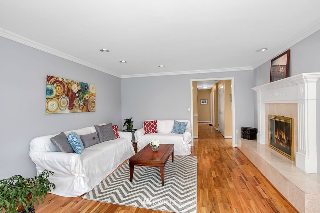 Staged living room with white sofas, hardwood floors, and a white fireplace.