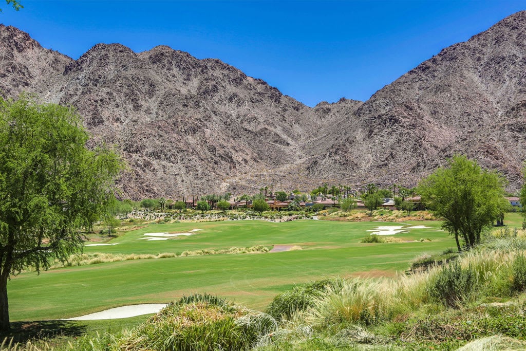 A lush green golf course with a fairway, bunkers, and a flag in the foreground.