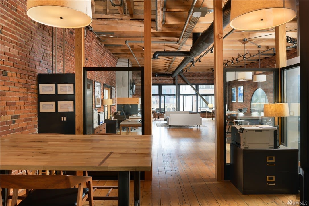 Spacious loft featuring warm wood tones, brick walls, and a view into a modern living space.