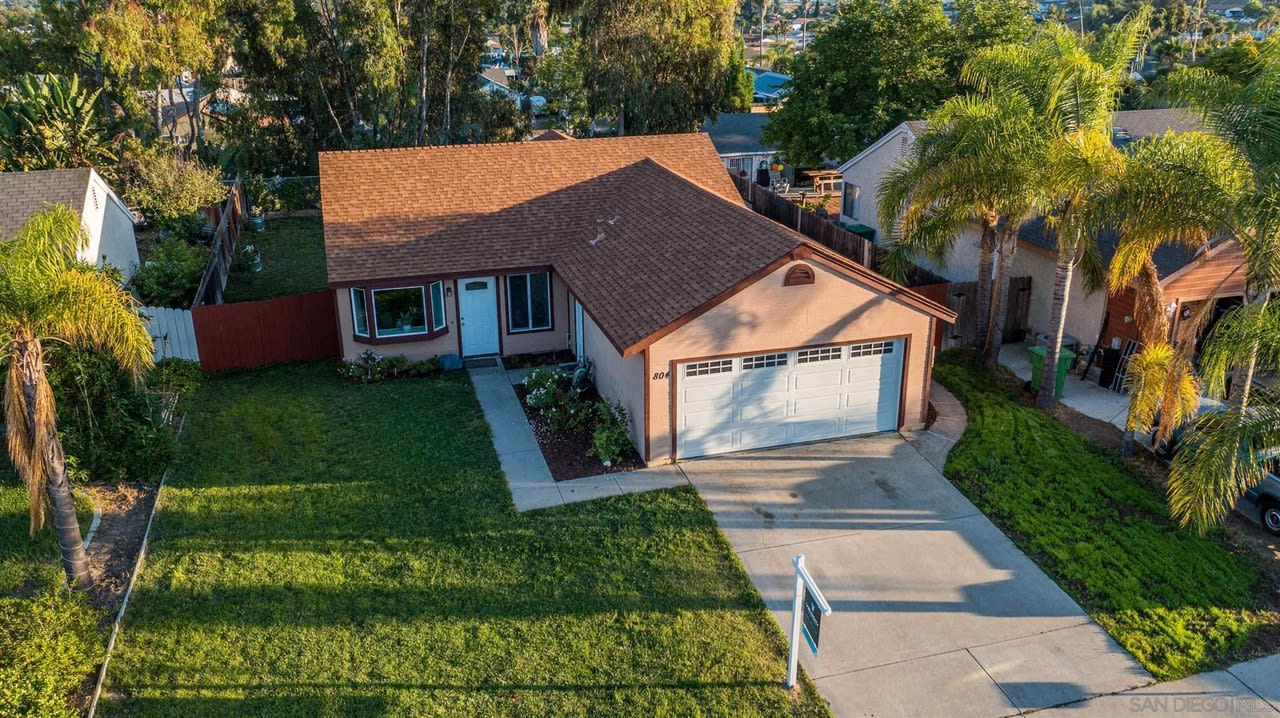 Aerial view of a single-story house with a broad lawn, double garage, and surrounding palm trees.
