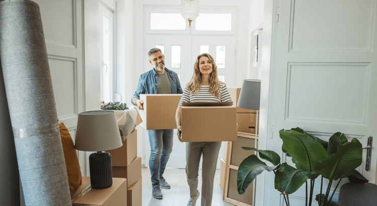 A couple carrying boxes into their new home, depicting the moving process. 