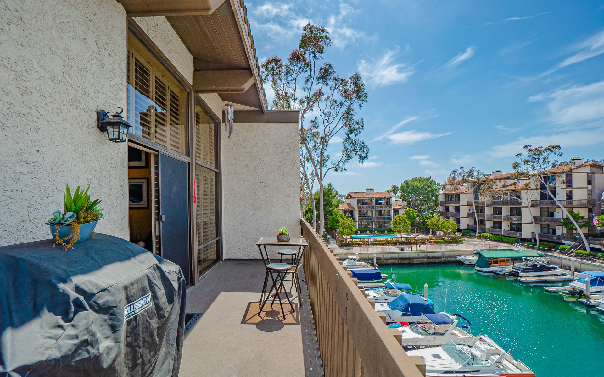 Condo balcony overlooking a marina, with boats, patio seating, and a covered grill.