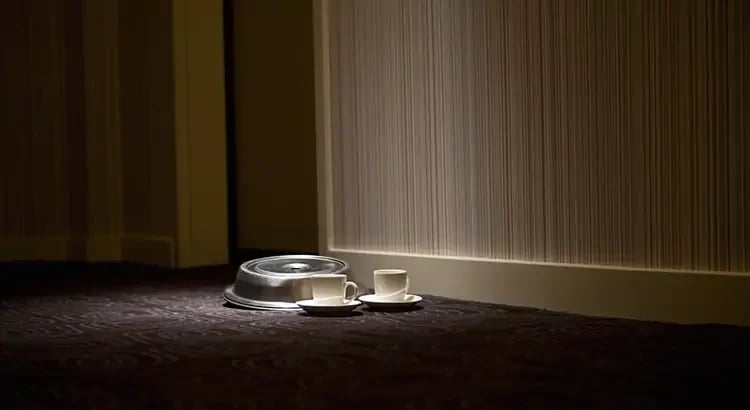 The hallway is dimly lit, with a focused light source creating a spotlight effect on the items placed on the floor. The overall ambiance is serene and somewhat somber, with shadows adding depth to the scene.