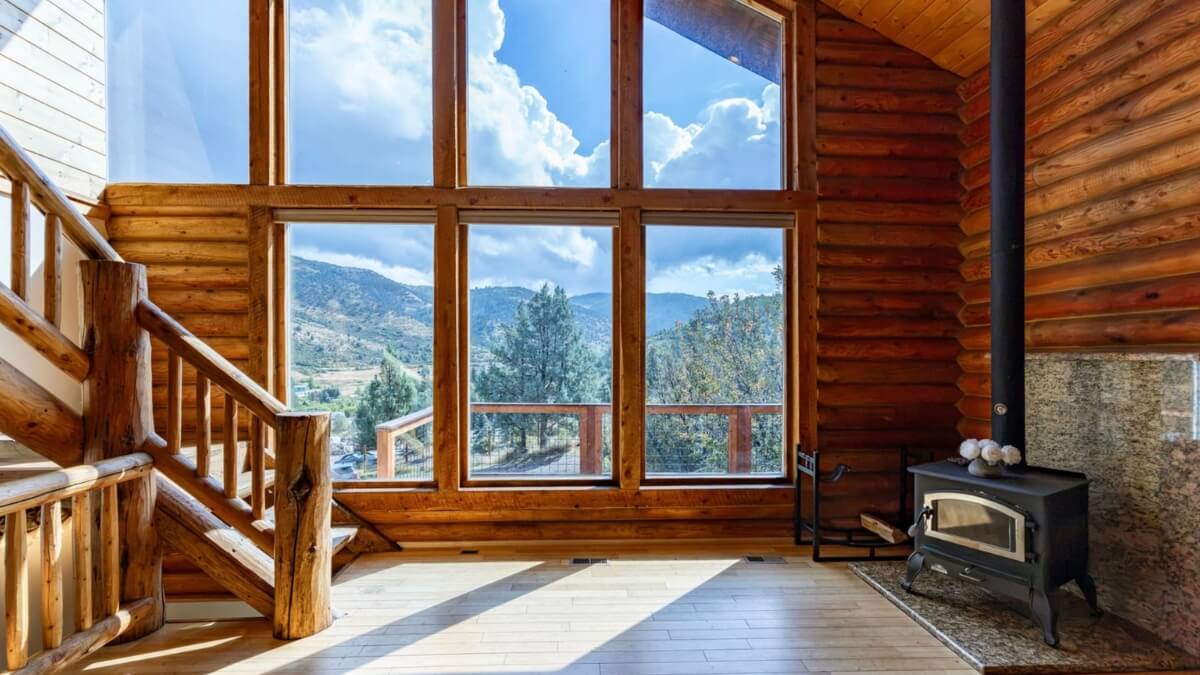 Log-cabin living room with a timber staircase, mountain-view windows, and a wood-burning stove.