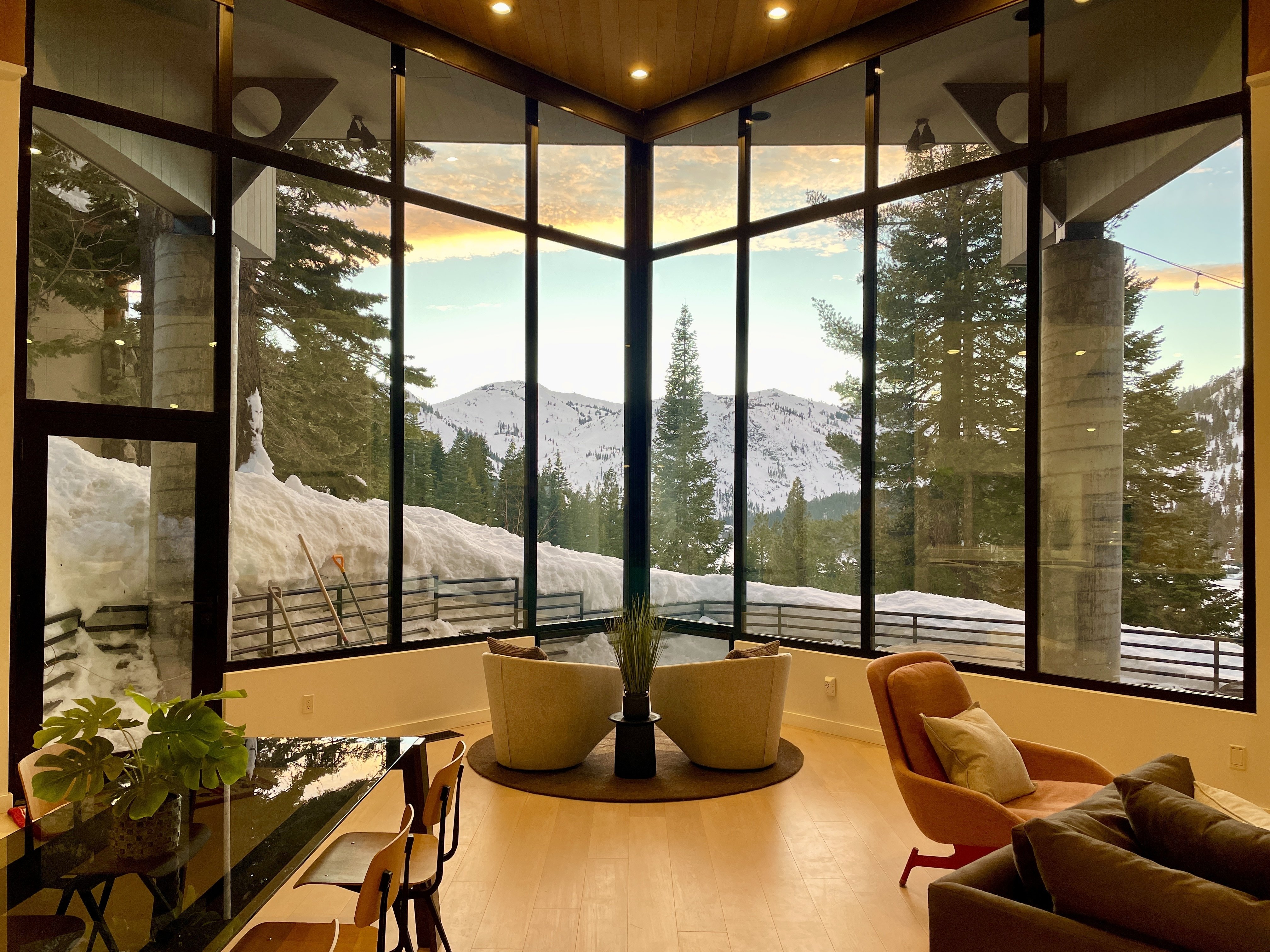 Furnished living room with floor-to-ceiling windows overlooking snowy mountains and evergreen trees.