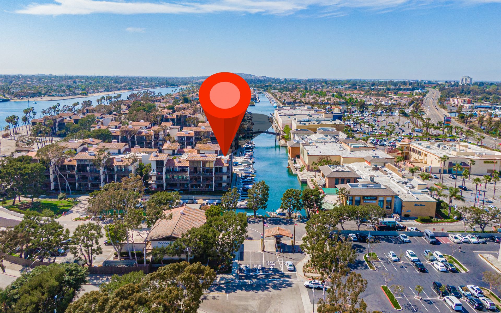 Aerial view of waterfront condominiums beside a marina canal, marked by a red location pin.