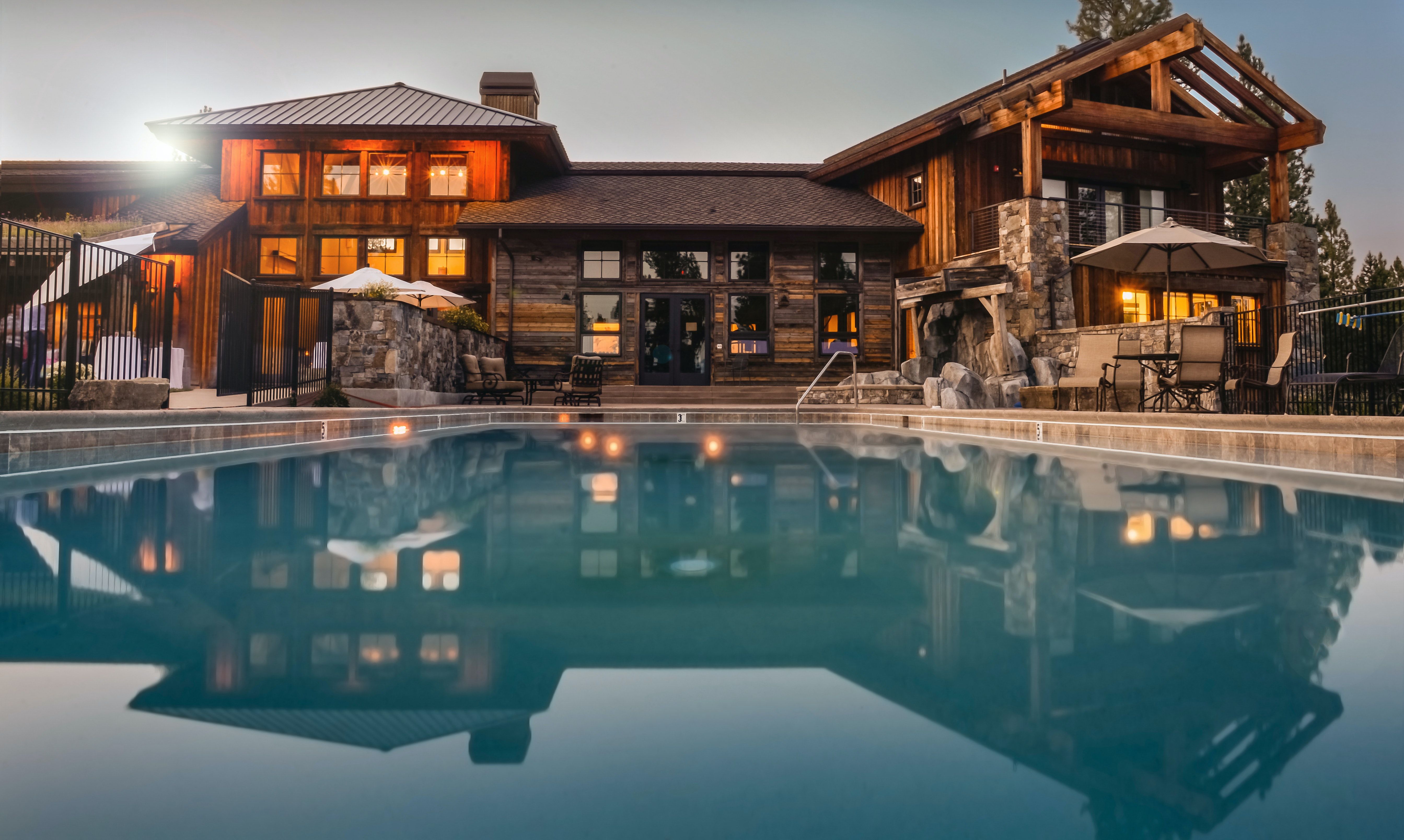 Rustic timber-and-stone luxury home with a swimming pool reflecting its illuminated facade.