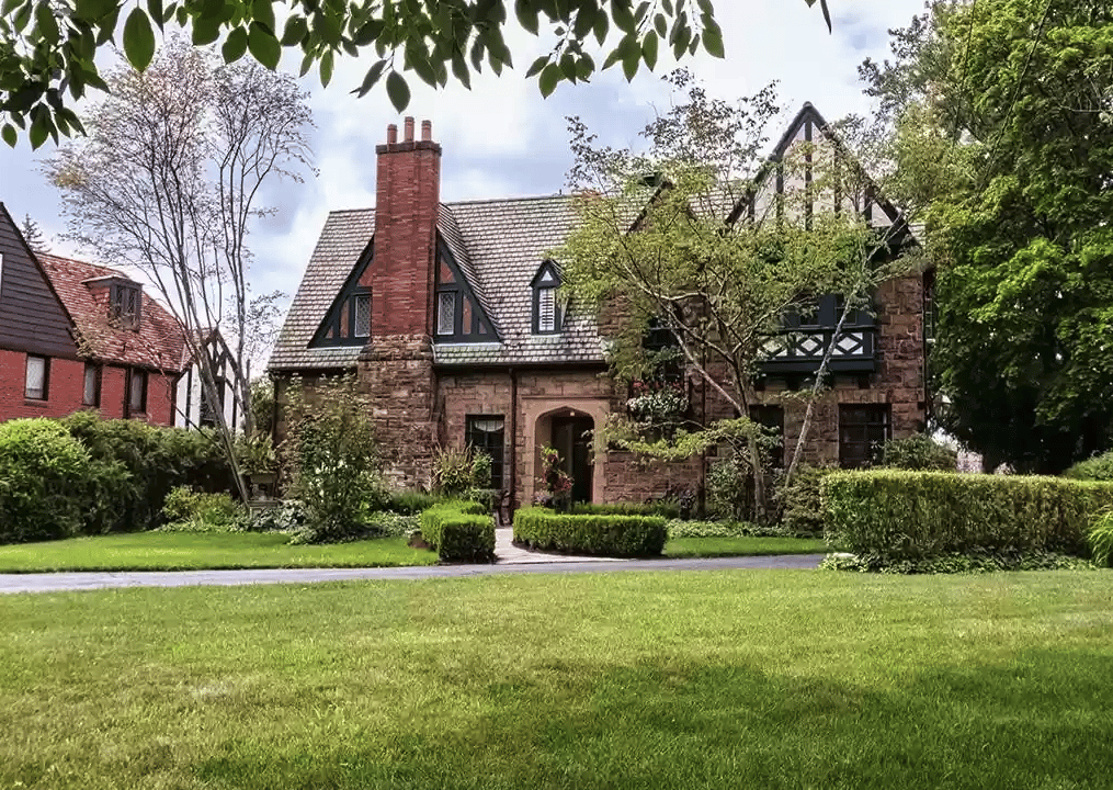 Tudor-style stone house with steep gables, a tall brick chimney, and a manicured lawn.