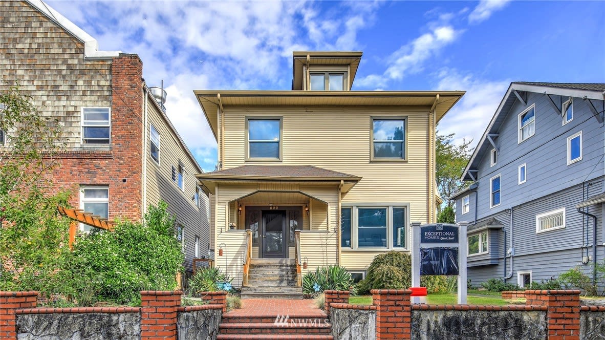 Tan two-story house with a covered entry, front steps, and a stone-and-brick front wall.