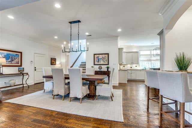 Dining room with a dark wood table and chandelier, open to a bright white kitchen.
