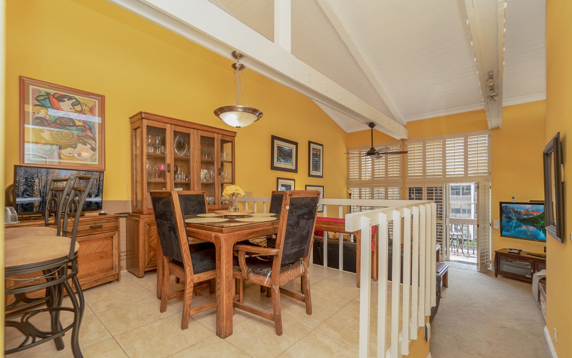 Dining area with a wooden table, glass-front cabinet, and vaulted ceiling with exposed beams.