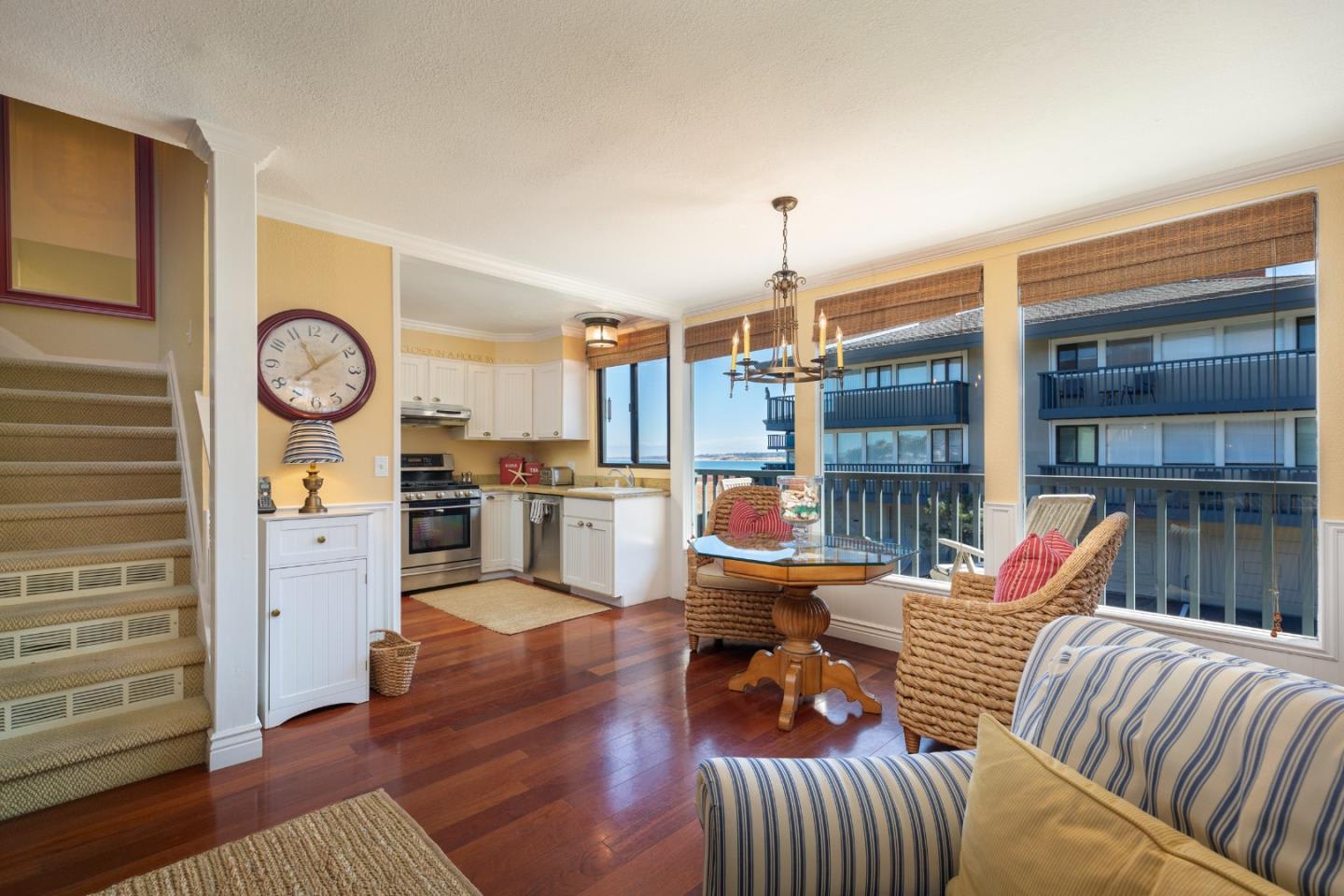 Open-plan living room and kitchen with wicker seating and water visible through large windows.