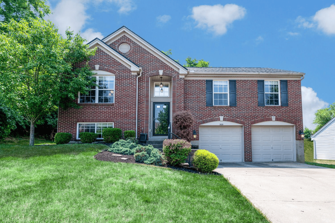 A brick home with two garages and a driveway. There are trees and bushes surrounding the house.