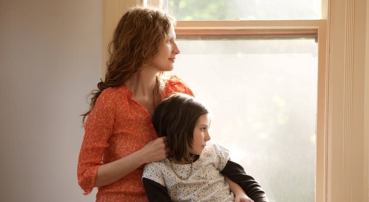 A woman sitting with a child, both facing a window, portraying a calm and nurturing scene. The sunlight coming in creates a warm and inviting atmosphere.