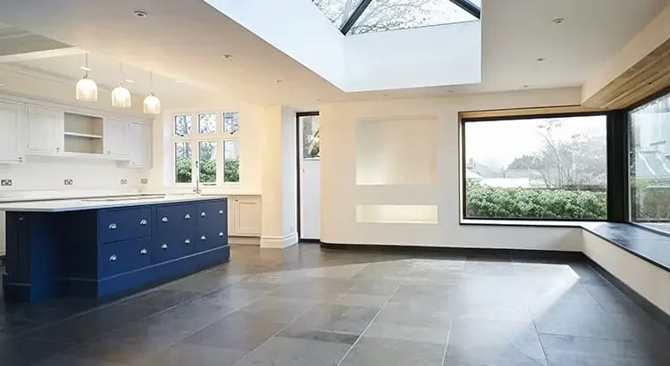 An interior view of a modern kitchen and living area. The space is open and bright, featuring large windows, a kitchen island, and contemporary decor.