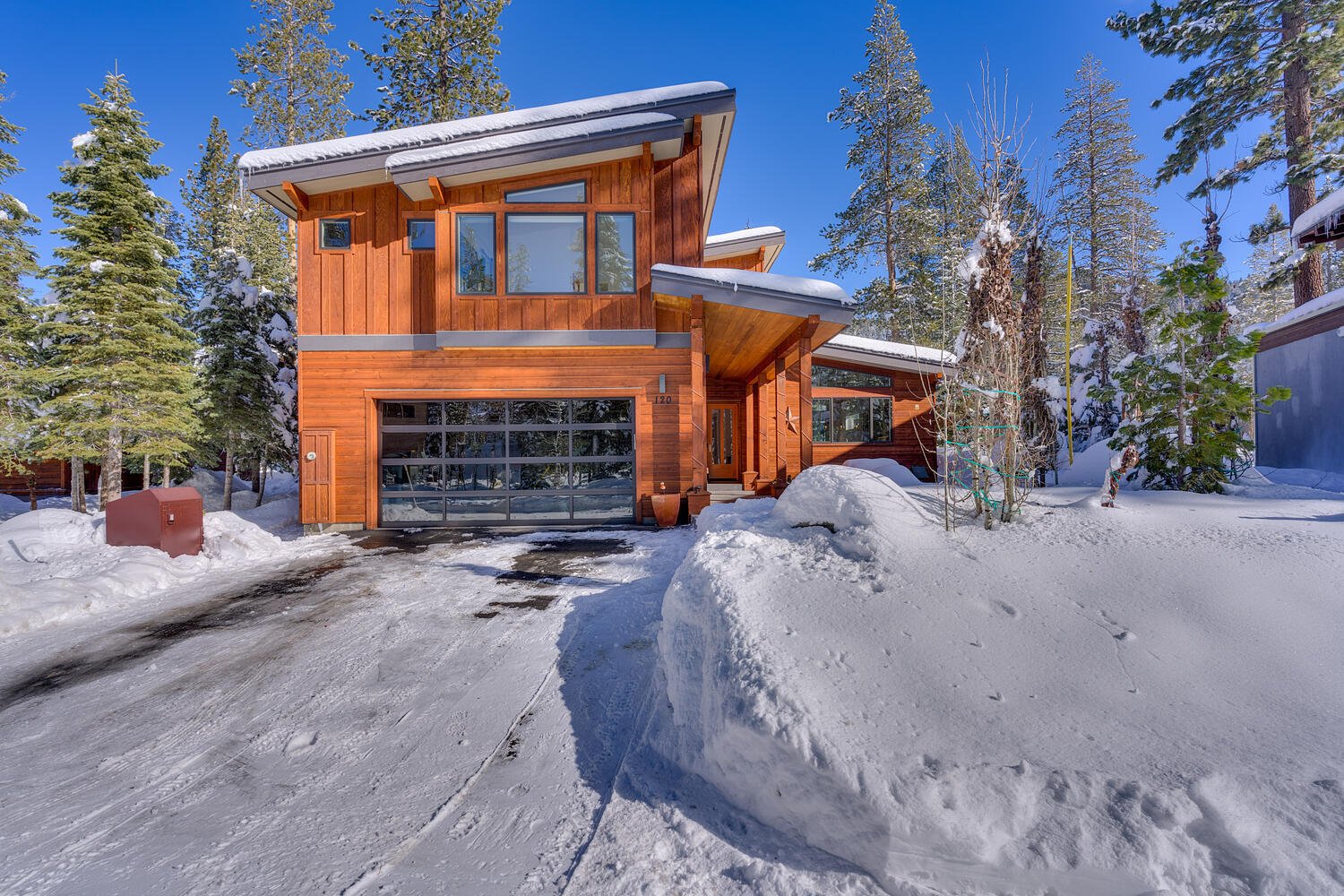 Modern wood-sided home with a glass garage door and snowbanks along the driveway.