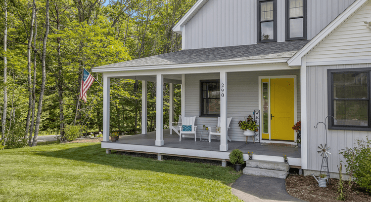 New construction, modern home with yellow door flying the American flag with a cozy front porch and welcome sign