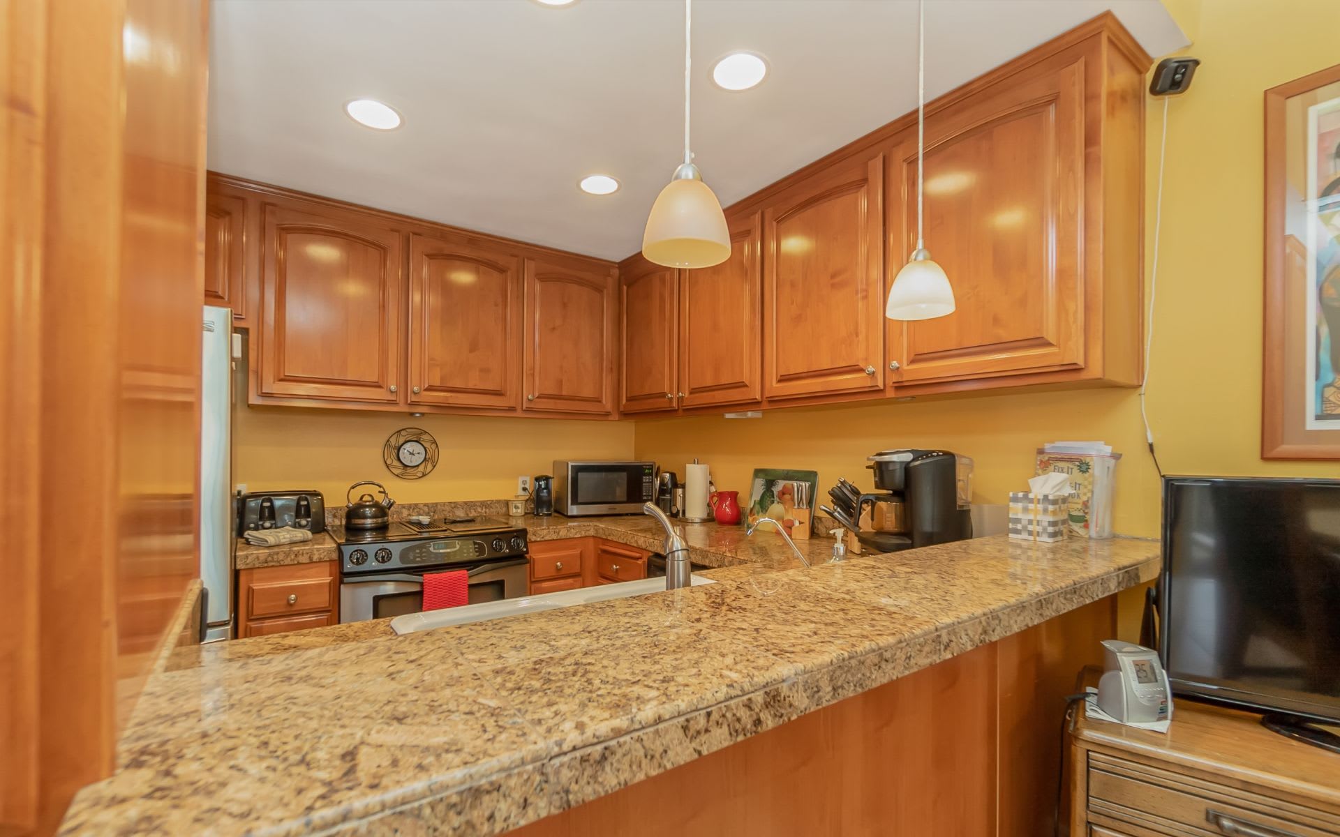 Kitchen with honey-colored wood cabinets, speckled stone counters, and a long breakfast bar.