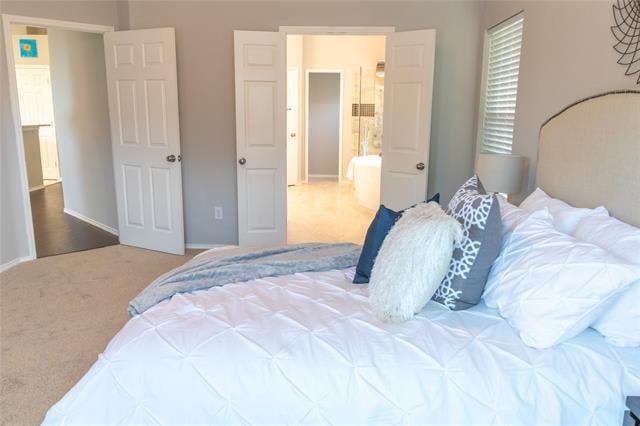Bright bedroom with white bedding, layered blue pillows, and open doors to an adjoining bathroom.