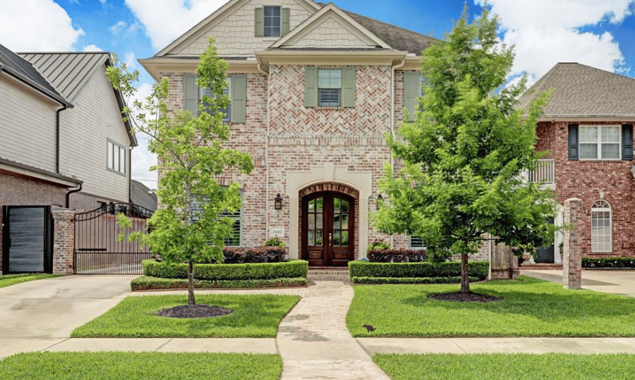 A large two-story brick house with a black slate roof, a front yard, a walkway, and an attached garage on the left.