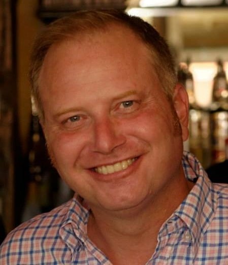 Trevor Spear smiling in a plaid shirt.