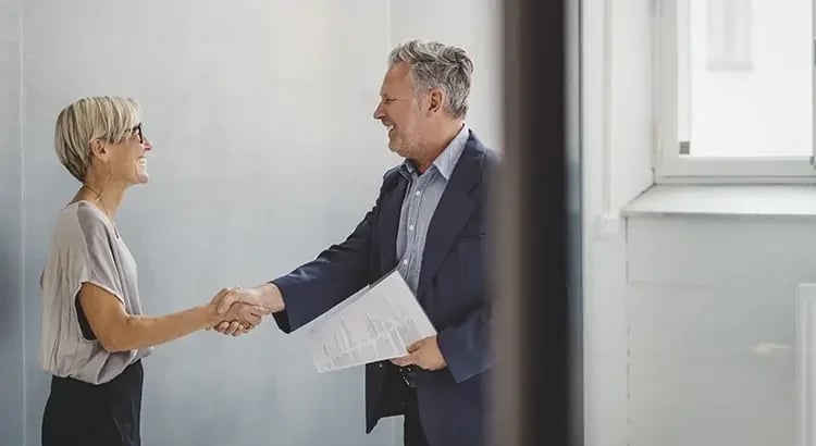 A professional setting where a man and a woman are shaking hands. They are both smiling, indicating a positive meeting or agreement.