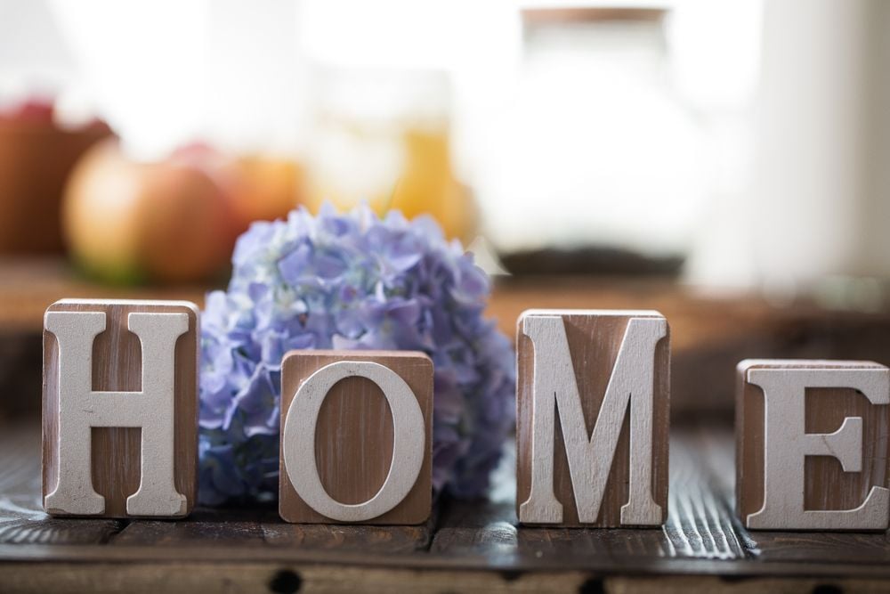 Wooden HOME letters sit beside purple hydrangeas on a dark table.