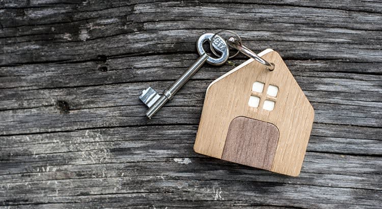 A key attached to a small wooden house model, symbolizing real estate, homeownership, or keys to a new home.