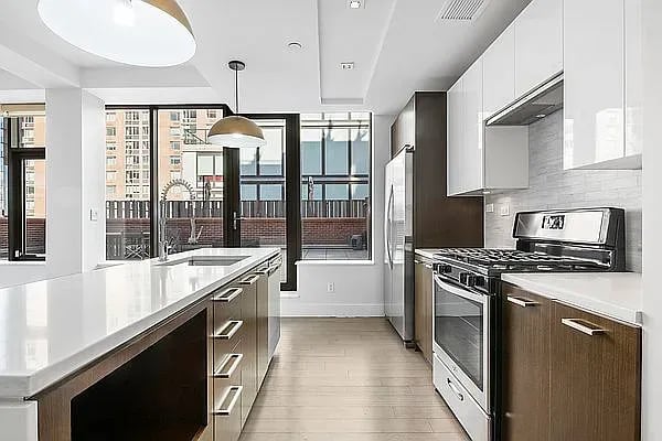Bright kitchen with a long white island, stainless appliances, and large windows.