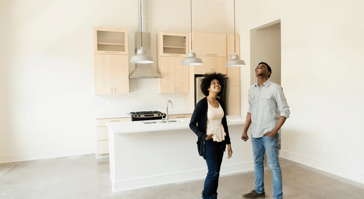 A couple inspecting a new, modern kitchen in what appears to be an empty or newly purchased home. The kitchen is minimalistic and contemporary.