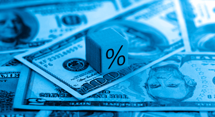 A blue block featuring a percent sign rests atop a stack of money, symbolizing financial growth or interest rates.