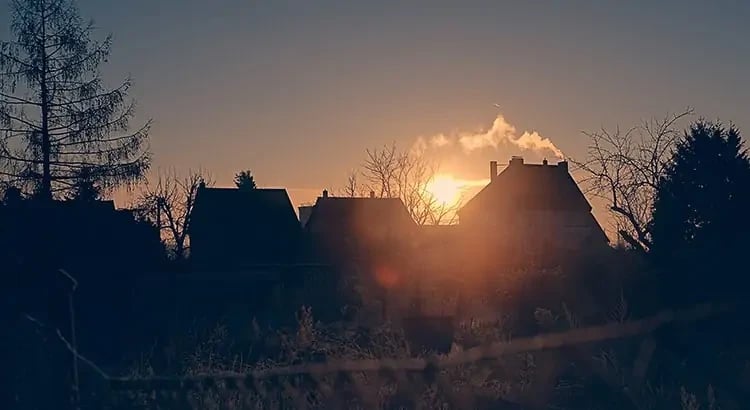  a sunset scene with silhouettes of houses and trees against an orange sky. The image conveys a peaceful and picturesque evening.