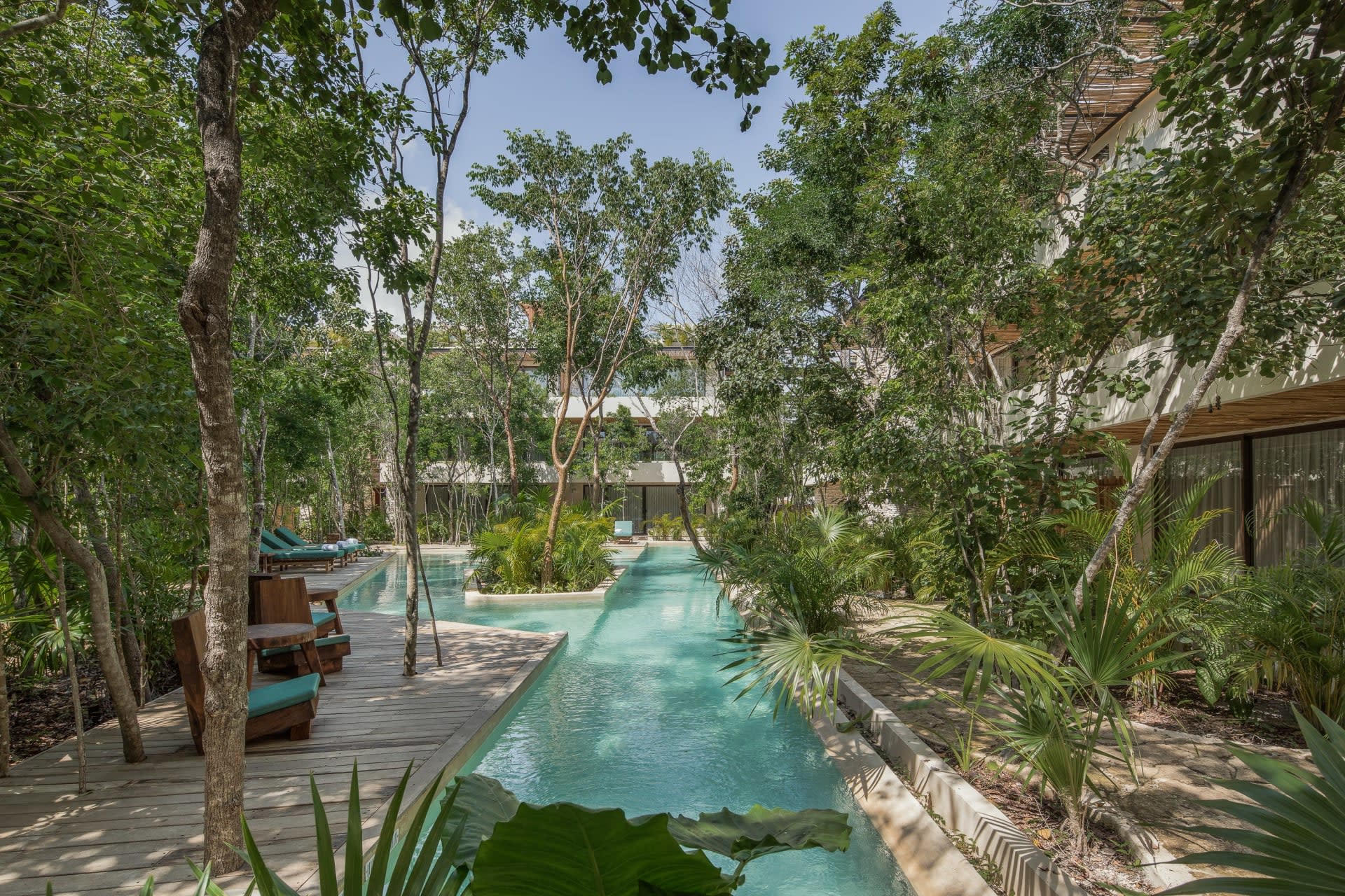 Courtyard pool winding between wooden decks, teal lounge chairs, and dense tropical greenery.