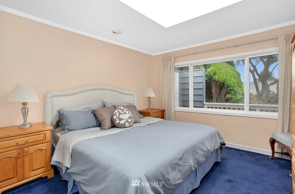 Bedroom with a large bed, blue carpet, and a wide window overlooking greenery.