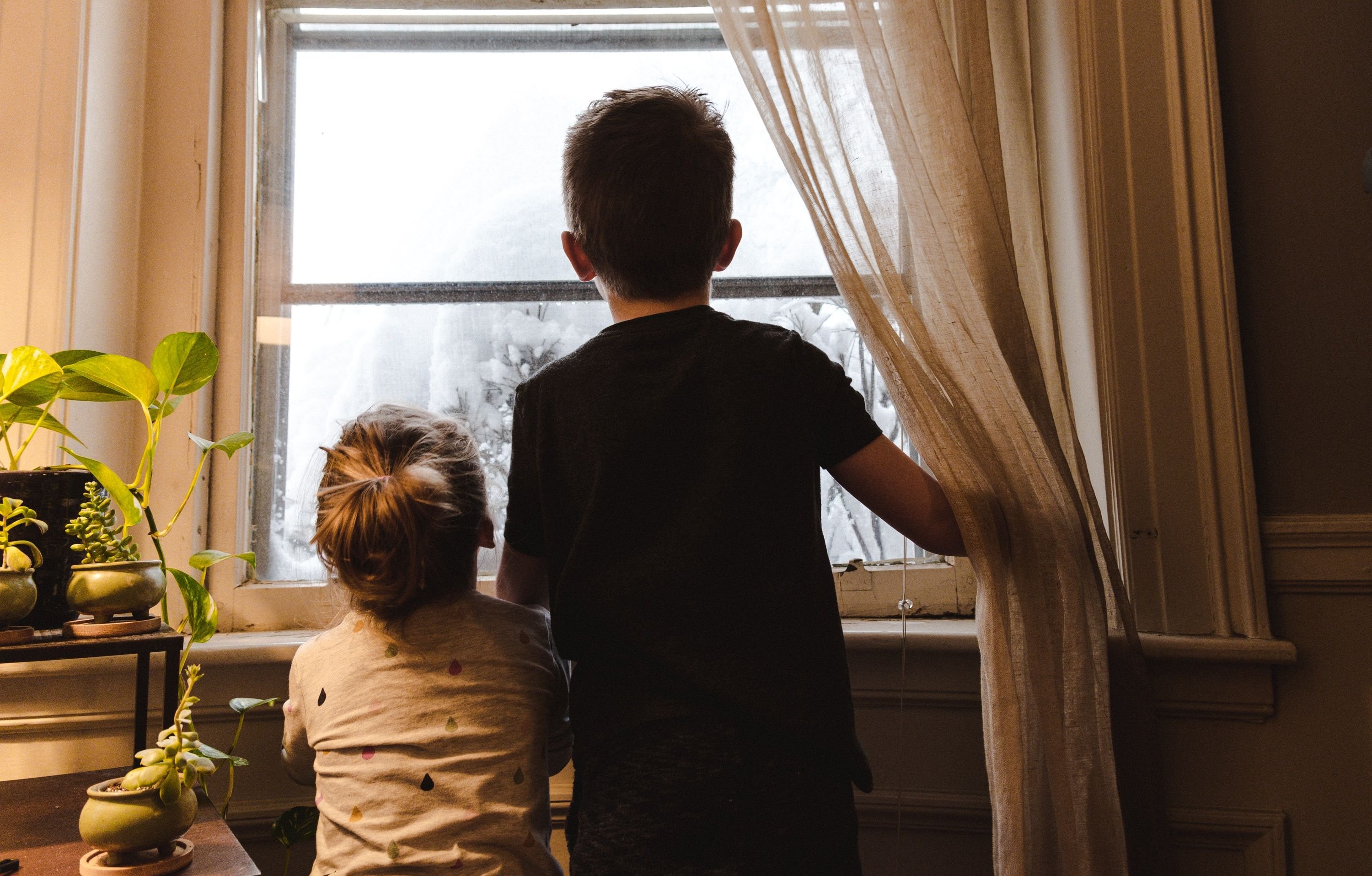 An adult and child look out a window at snow-covered trees.