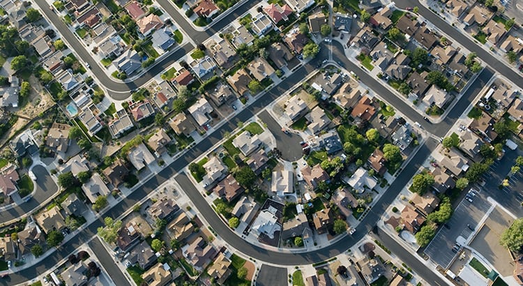 An aerial view of a residential neighborhood, showing a pattern of streets, houses, and green spaces. The image captures the layout and density of the neighborhood.